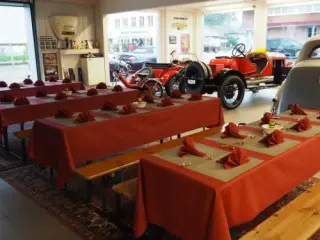 Festlich gedeckte Tische mit roten Tischtüchern in der Ausstellungshalle, dahinter ein roter Rennwagen