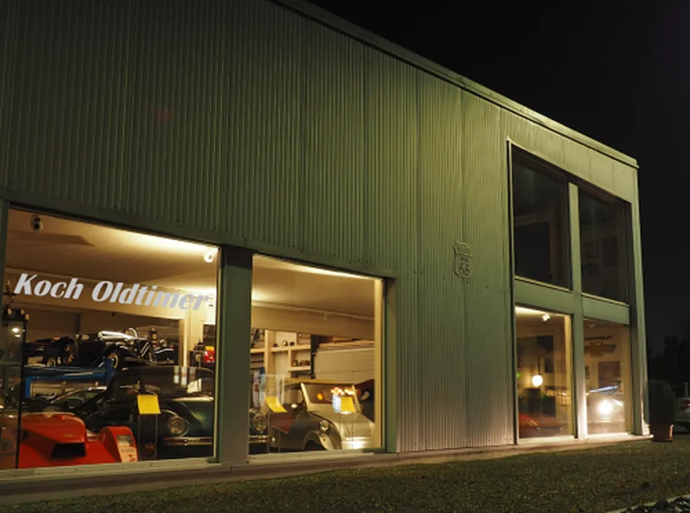 Die beleuchtete Ausstellungshalle von Koch Oldtimer bei Nacht, im Schaufenster der Schriftzug «Koch Oldtimer»