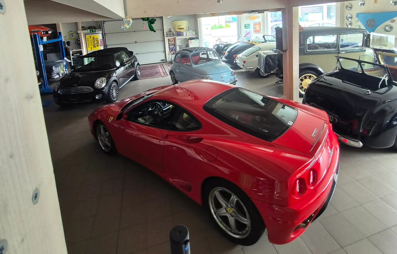 Blick in die Ausstellungshalle: ein roter Ferrari, ein schwarzes Mini Cabriolet, ein hellblauer Fiat 500 und weitere Fahrzeuge