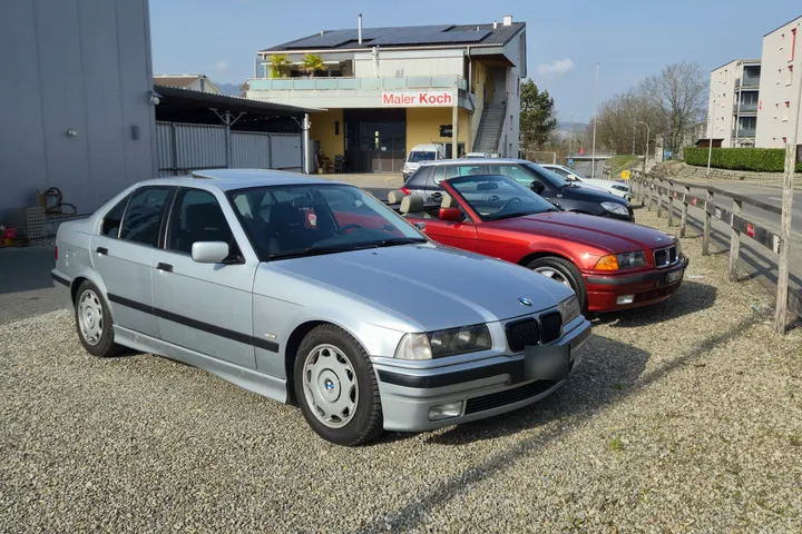 Silberne BMW-Limousine und rotes BMW-Cabriolet auf dem Kiesplatz vor der Halle